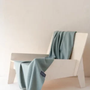 TBCo Lambswool Small Blanket in Sage Melange draped elegantly over white chair, showcasing soft texture and fringed detail
